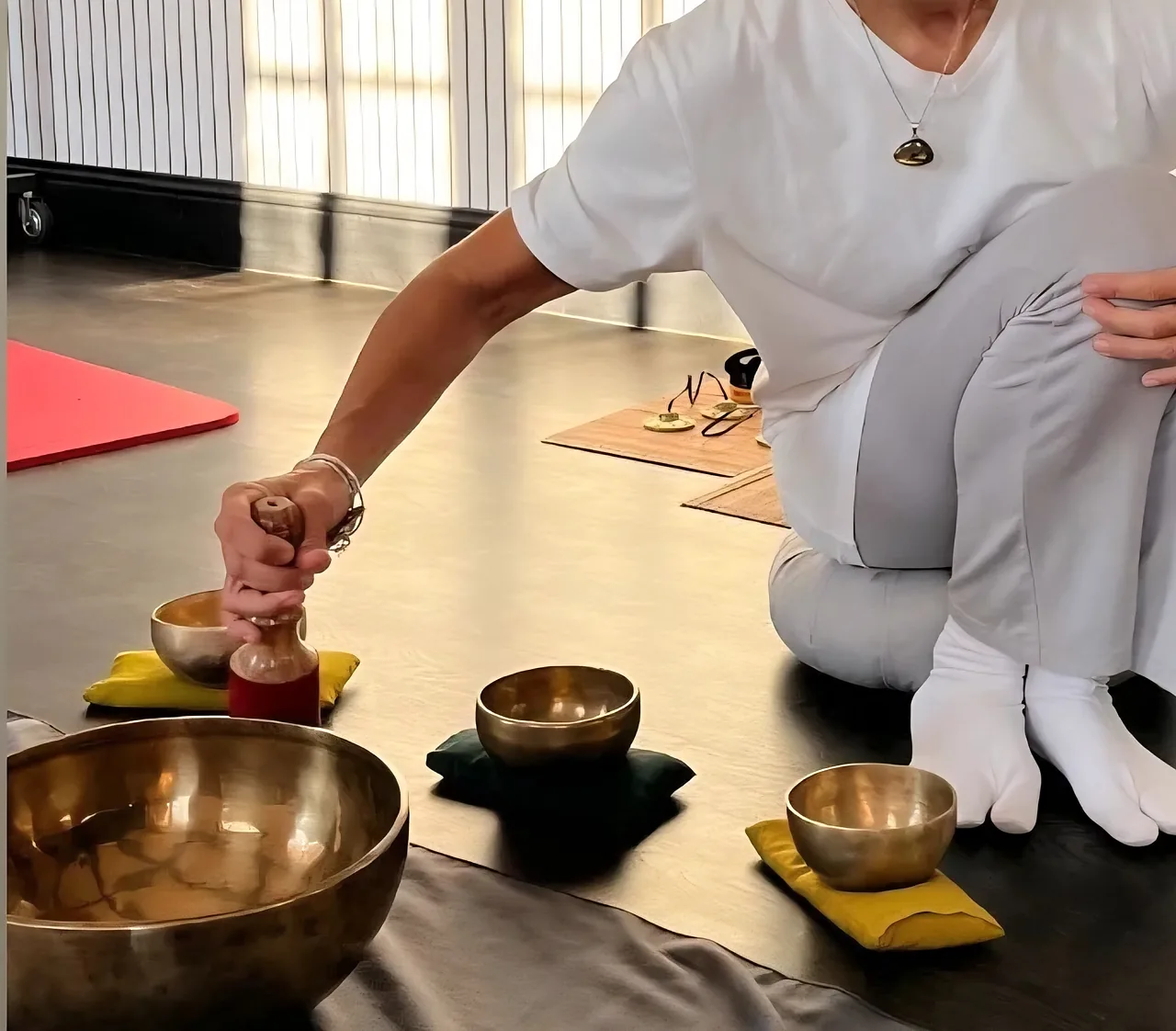 Les mains de Christel Louvet tenant un maillet au-dessus d’un bol chantant, entourée de bols tibétains posés sur des coussins